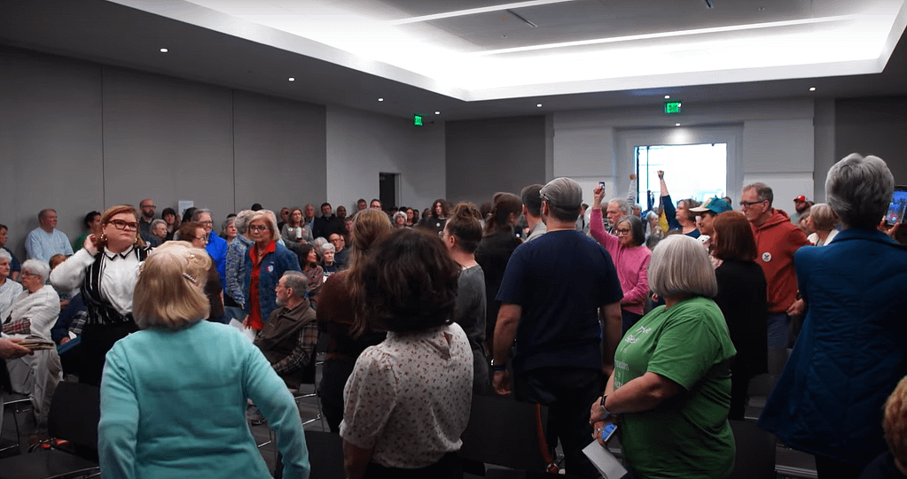 large room full of people standing up, some with fists in the air 