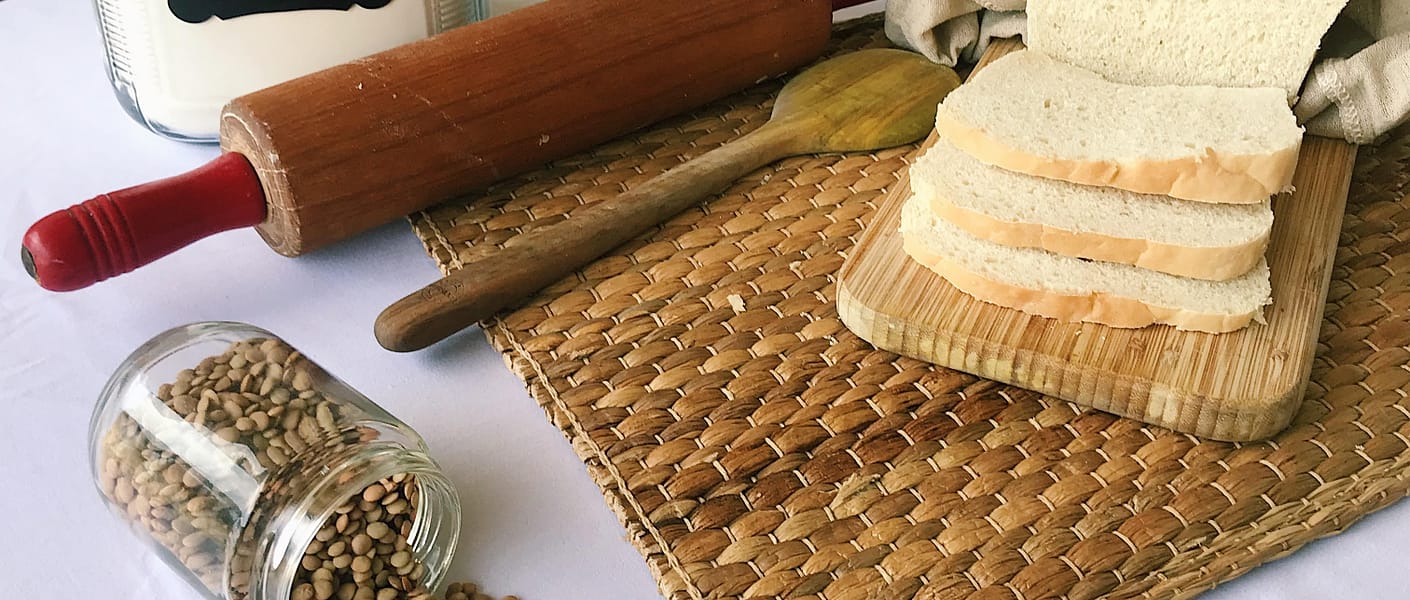 bread, lentils, flour jar, rolling pin on table with bamboo mat under them