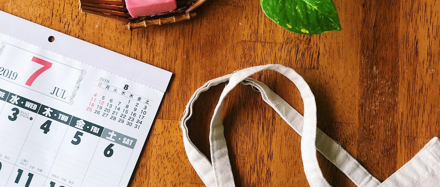 pink soap bar, calendar, plant and reusable canvas bag on top of wooden table