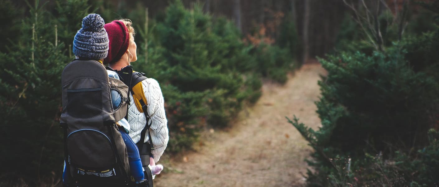 blond woman with baby in carrier on her back walking down path