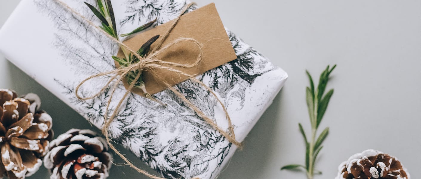 presents wrapped in white wrapping paper with brown tags, string, pinecones and greenery scattered around