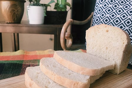 sliced white bread sitting on cutting board with plants and chair in background