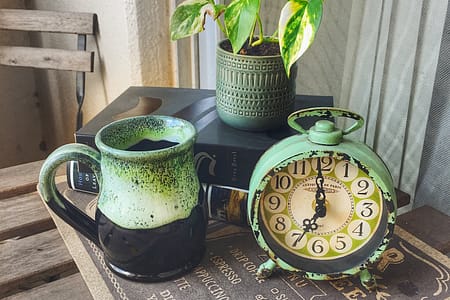 aqua alarm clock, light blue and black pottery mug and small plant sitting on table on balcony