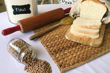 bread, lentils, flour jar, rolling pin on table with bamboo mat under them