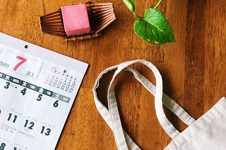 pink soap bar, calendar, plant and reusable canvas bag on top of wooden table