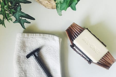 washcloth with a metal razor on top, bar of soap, green plant on white background