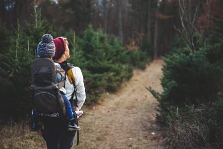 blond woman with baby in carrier on her back walking down path