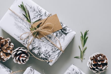 presents wrapped in white wrapping paper with brown tags, string, pinecones and greenery scattered around