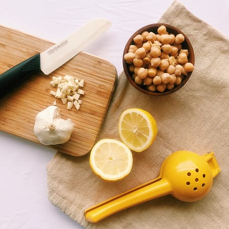 bowl of chickpeas, lemon cut in half, lemon squeezer, knife and chopped garlic on cutting board